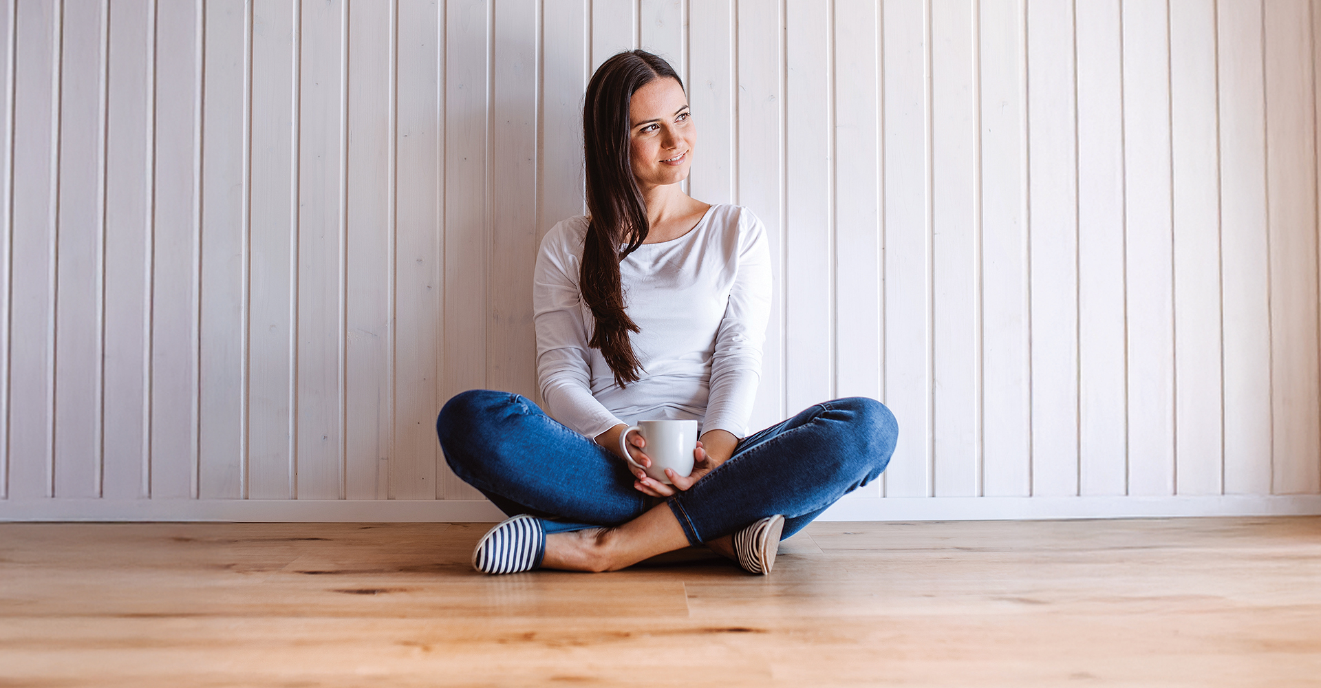 Woman sitting on a hardwood floor with a coffee mug in her hand.