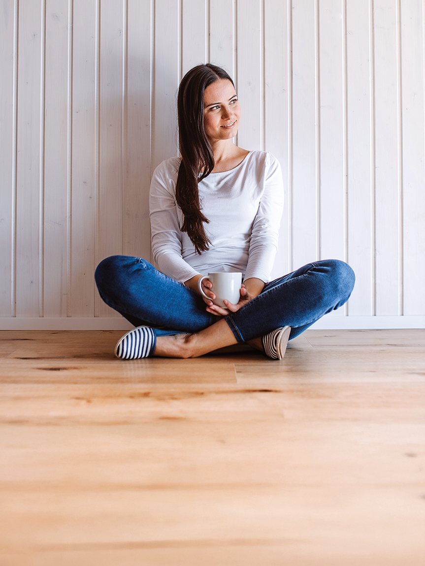 Woman sitting on a hardwood floor with a coffee mug in her hand.